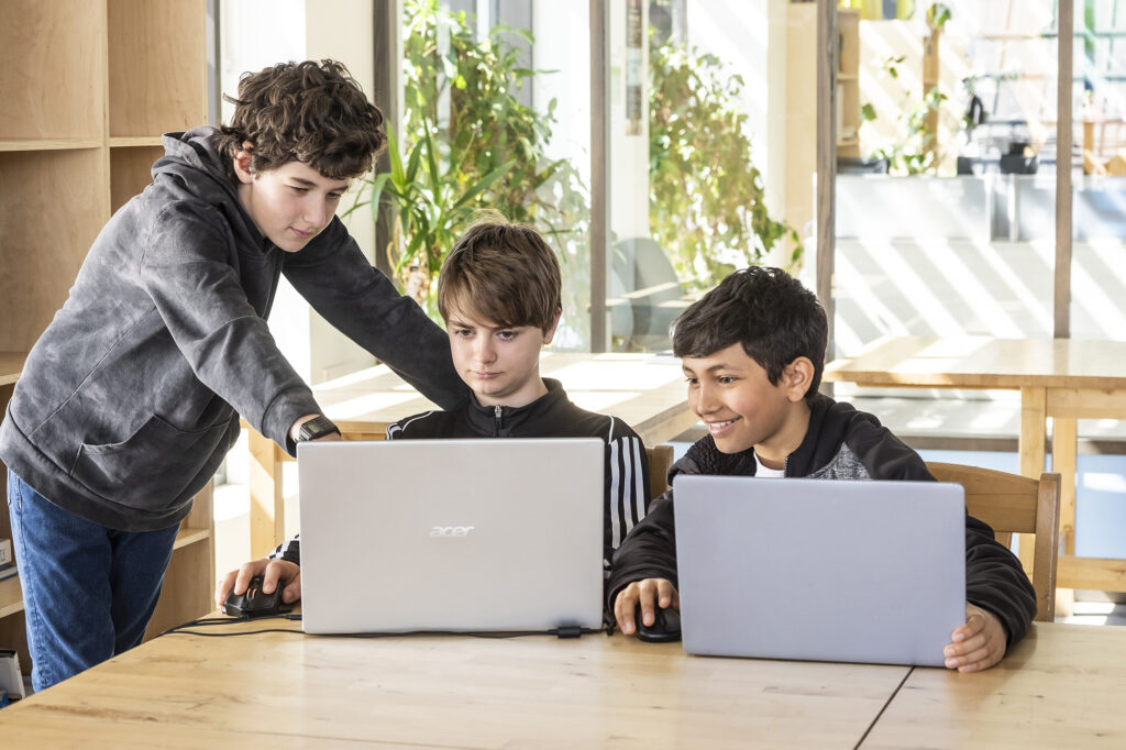 Trois étudiants étudiant devant un ordinateur portable et souriant